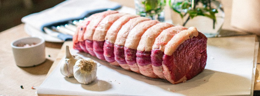 Goodwood organic grass-fed gammon joint, surrounded by decorative Christmas holly, displayed on a chopping board at Goodwood Farm Shop.