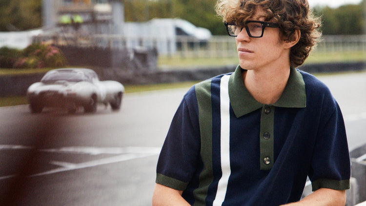 Female model wearing white overalls sat in Pit Lane, male model wearing Revival polo shirt