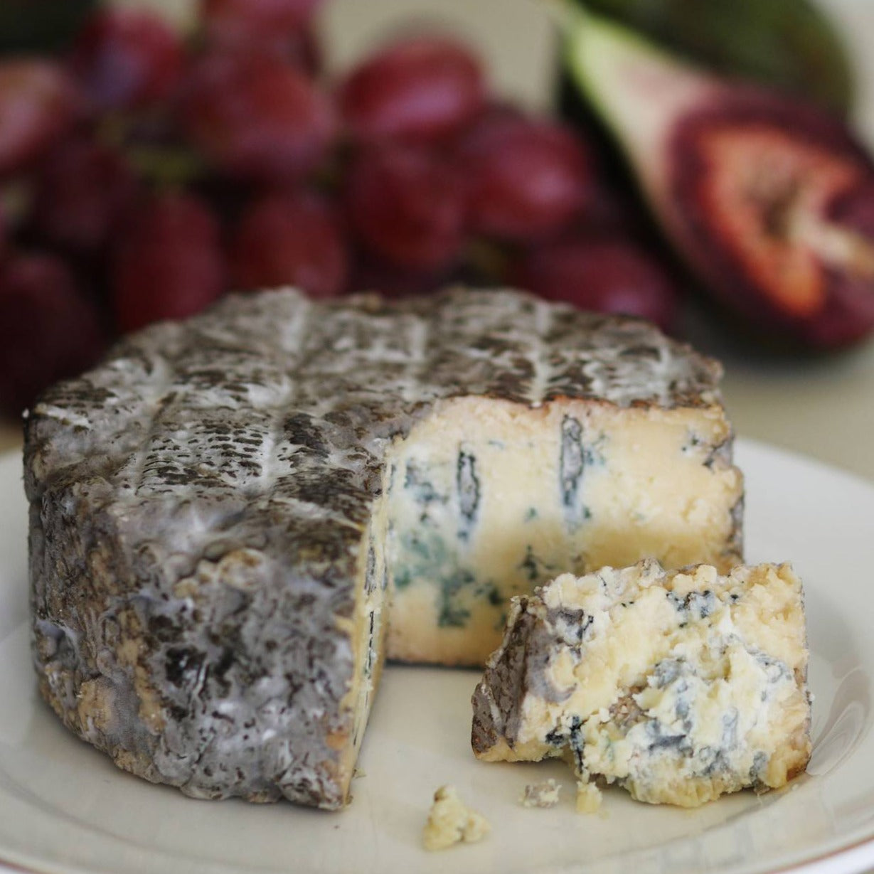 Goodwood's Molecomb Blue soft blue veined cheese, with a dark smoky grey crust, displayed as part of a cheese board.