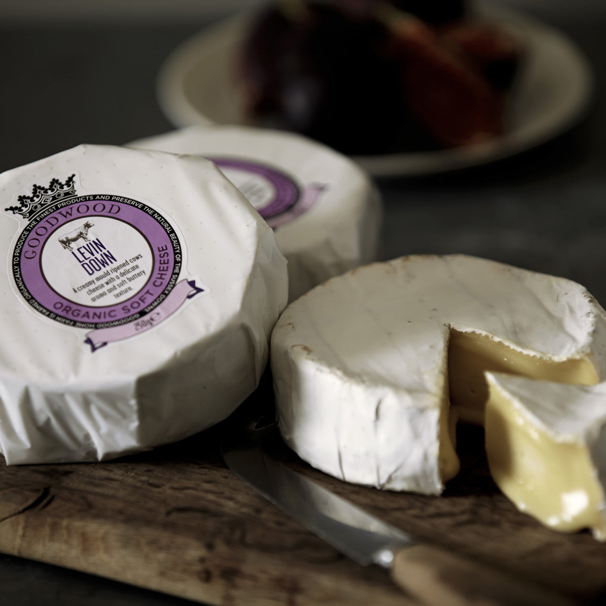 One packaged and one sliced Levin Down soft and creamy white cheese, displayed on a cheese board.