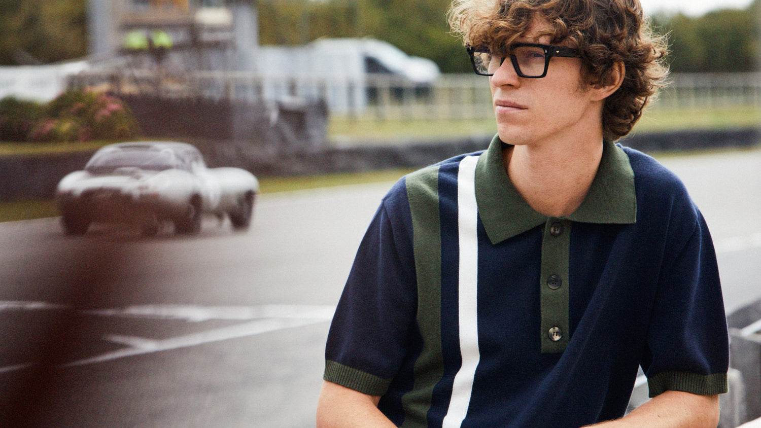 Female model wearing white overalls sat in Pit Lane, male model wearing Revival polo shirt