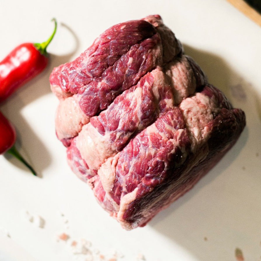 A top down view of Goodwood Farm Shop's organic beef brisket, shown on a chopping board with red peppers and garlic cloves.