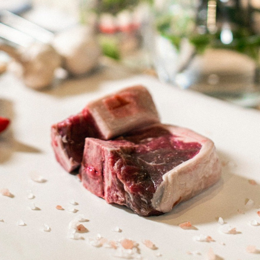 A side view of Goodwood's grass-fed organic lamb loin chop, displayed on a chopping board with red peppers and garlic cloves.