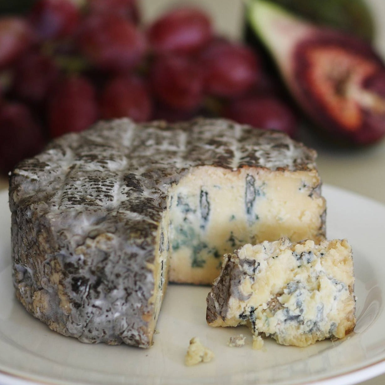 Goodwood's Molecomb Blue soft blue veined cheese, with a dark smoky grey crust, displayed as part of a cheese board.