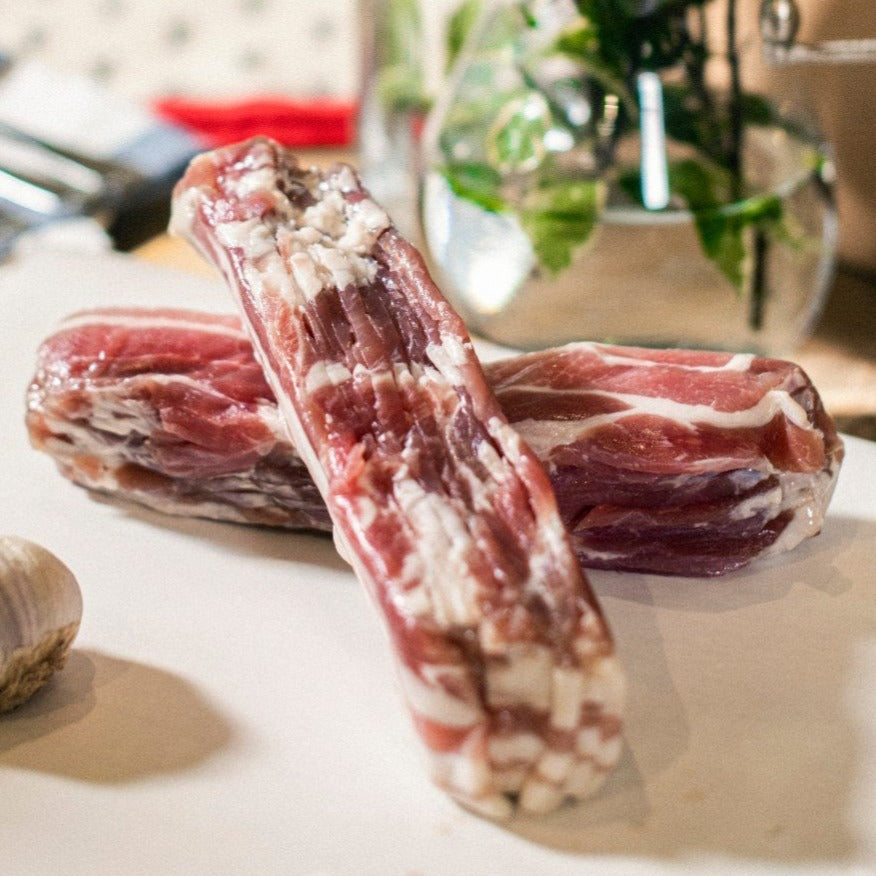Two sets of Goodwood's organic pork streaky bacon rashers, shown on a chopping board at Goodwood Farm Shop.