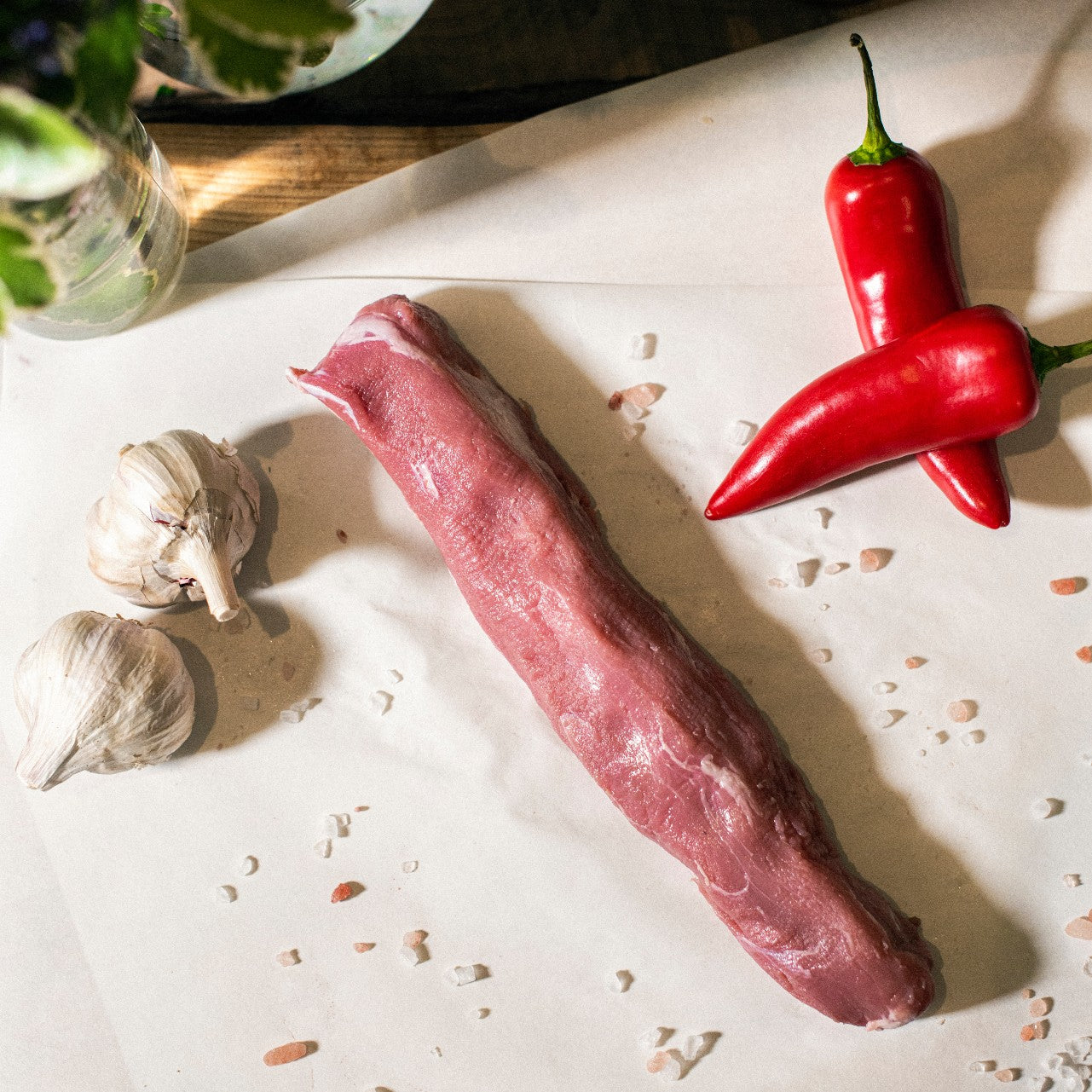 Goodwood's organic grass-fed pork tenderloin, displayed on a chopping board with garlic cloves and red peppers.