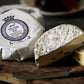 One packaged and one sliced Molecomb Blue soft blue veined cheese, displayed on a cheese board.